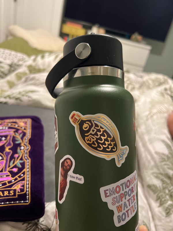 One of The Quirky Cup Collection stickers in use. On an olive green waterbottle sits a gold holographic vinyl sticker of a soy sauce fish.