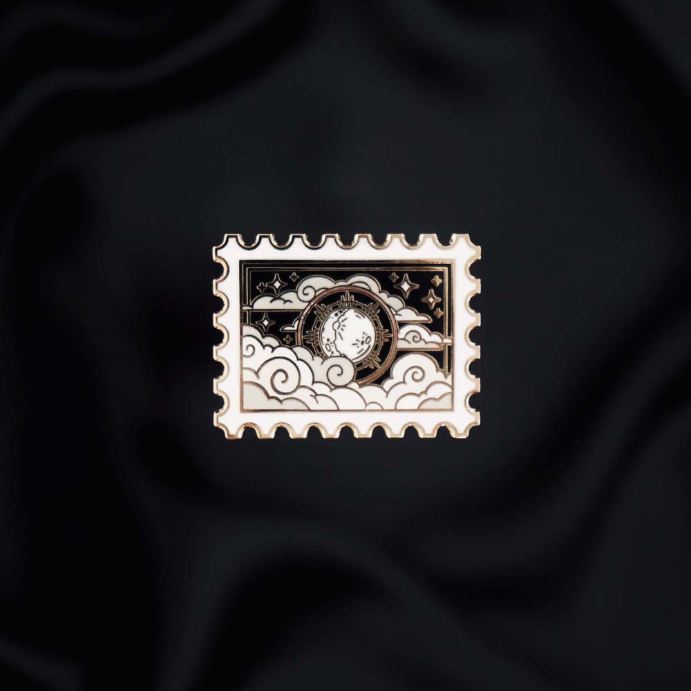 Dark Night- A The Quirky Cup Collective romantasy inspired enamel pin sits on a black background. The black and silver postage stamp enamel pin features moon, cloud and star motifs.