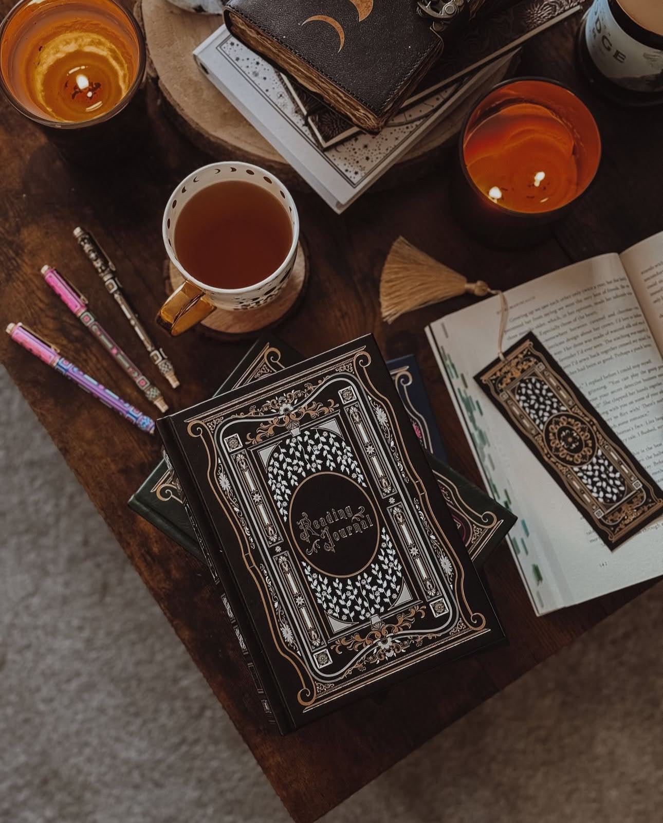 Ambassador image showing the black reading journal by The Quirky Cup Collective styled on a table surrounded by candles and pens.