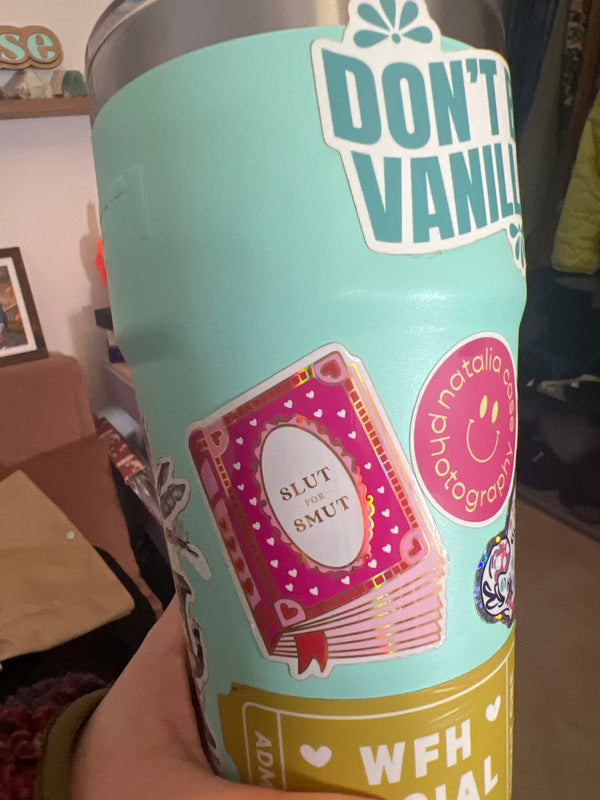 One of The Quirky Cup Collection vinyl stickers in use. On a mind green waterbottle sits one of the romantasy book inspired stickers- a pink book with the title 'slut for smut'