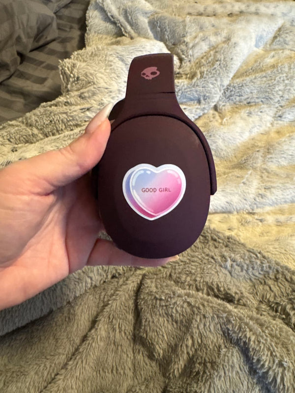 One of the The Quirky Cup Collection vinyl stickers in use. On a chocolate brown set of over ear headphones, a candy heart sticker that says 'good girl' is stuck to the side.