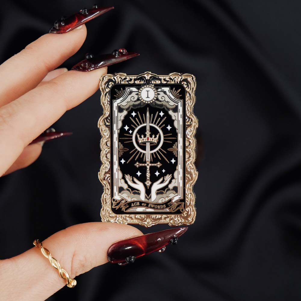 Gold and black crown tarot card enamel pin held by a hand against a dark background