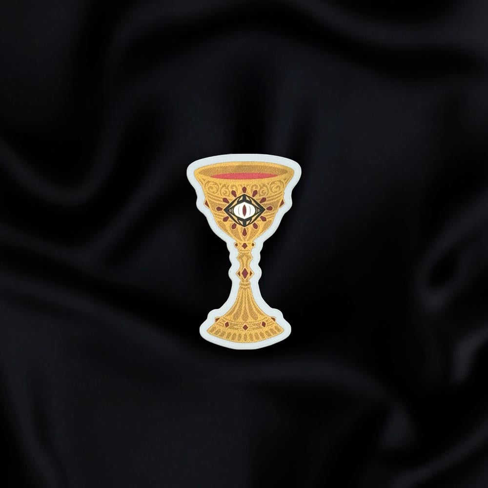 Blood Spilled- a fantasy vinyl sticker by The Quirky Cup Collective as part of the 'Serpents and Swords' collection- sits on a black fabric background. The book inspired sticker shows a goblet filled with blood with an eye motif on the front.