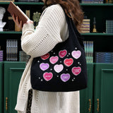 woman browses green book shelves and carries a black canvas tote bag covered in candy hearts and stars. The stars are in shades of purple, pink and red and refer to common romance fantasy book tropes