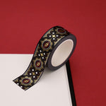 A close up of the Dragon Born washi tape by The Quirky Cup Collective. The roll of fantasy inspired washi tape is on the corner of a white journal on a red background. The bookish washi tape design is red and black with gold detailing- the intricate design showing a serpent eye.