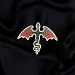 Dragon Rider- a fantasy vinyl sticker by The Quirky Cup Collective as part of the 'Serpents and Swords' collection- sits on a black fabric background. The fantasy book sticker shows a black and red dragon with gold detailing flying, as viewed from above.