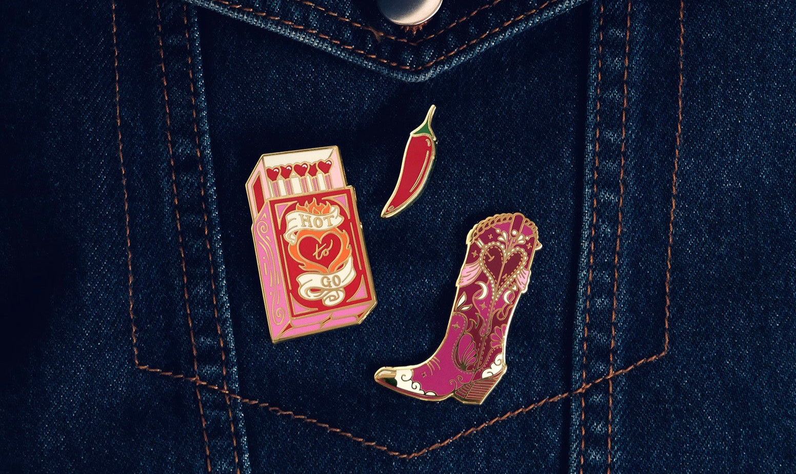 Three pins on a denim jacket: a box of hot sauce, a chili pepper, and a cowboy boot.