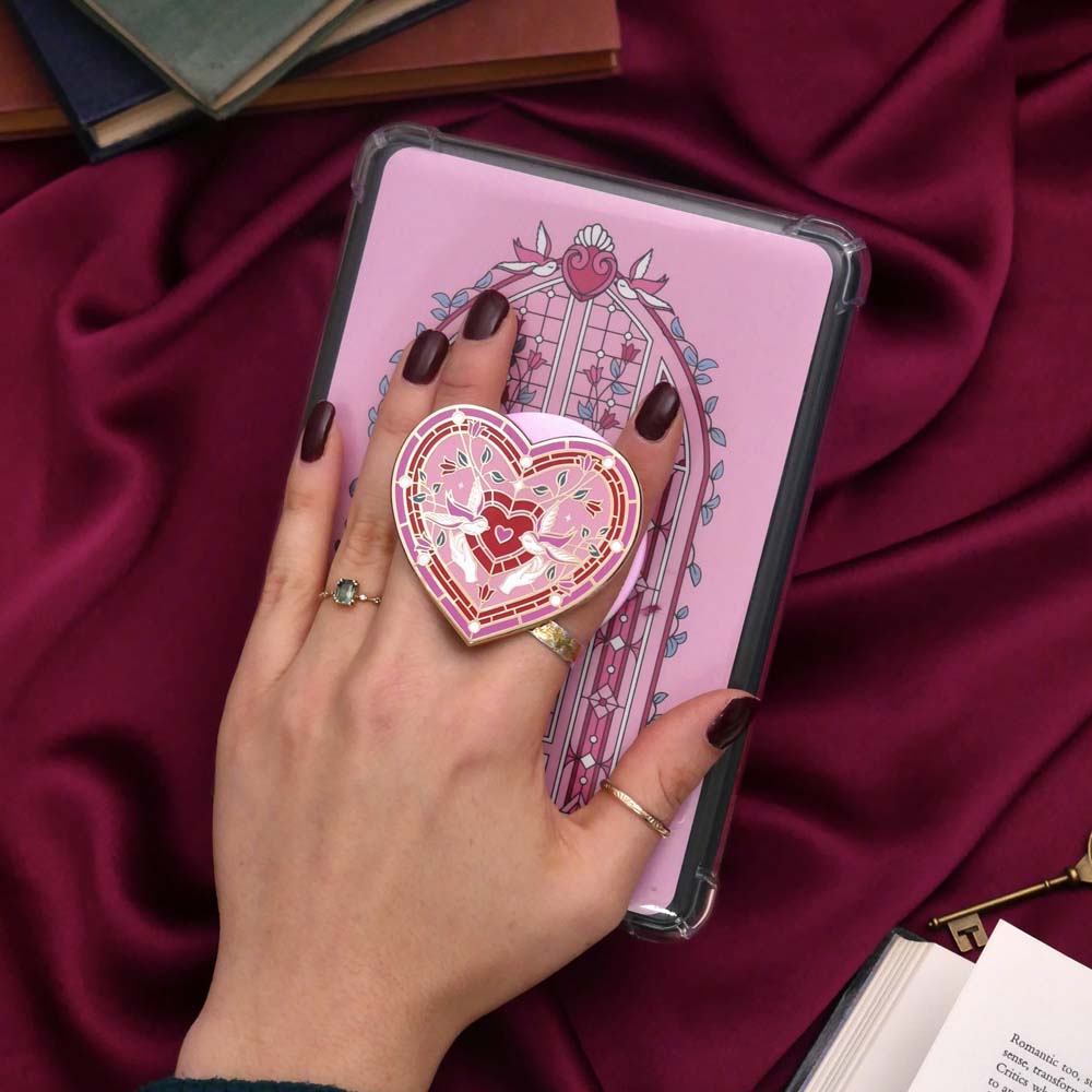 Heart-shaped decorative item held by a hand against a pink notebook on a red fabric background