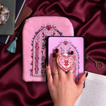 The Sugar & Spice e-reader bundle set is shown on a pink fabric background and  includes a velvet e-reader case, enamel clingie and kindle sticker insert. The design centers on a light pink stained glass arch design in shades of pink, red and green, the clingie featuring a heart and birds in a heart shaped design.