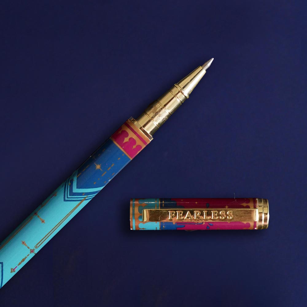 A detail shot of the engraved clip of the Fearless pen by The Quirky Cup Collective . The pink and blue pen sits on a blue background and sees 'Fearless' engraved into the clip.