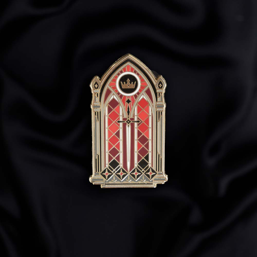 black red and gold window with sword and crown enamel pin held by a hand against a dark background