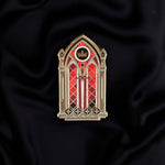 black red and gold window with sword and crown enamel pin held by a hand against a dark background