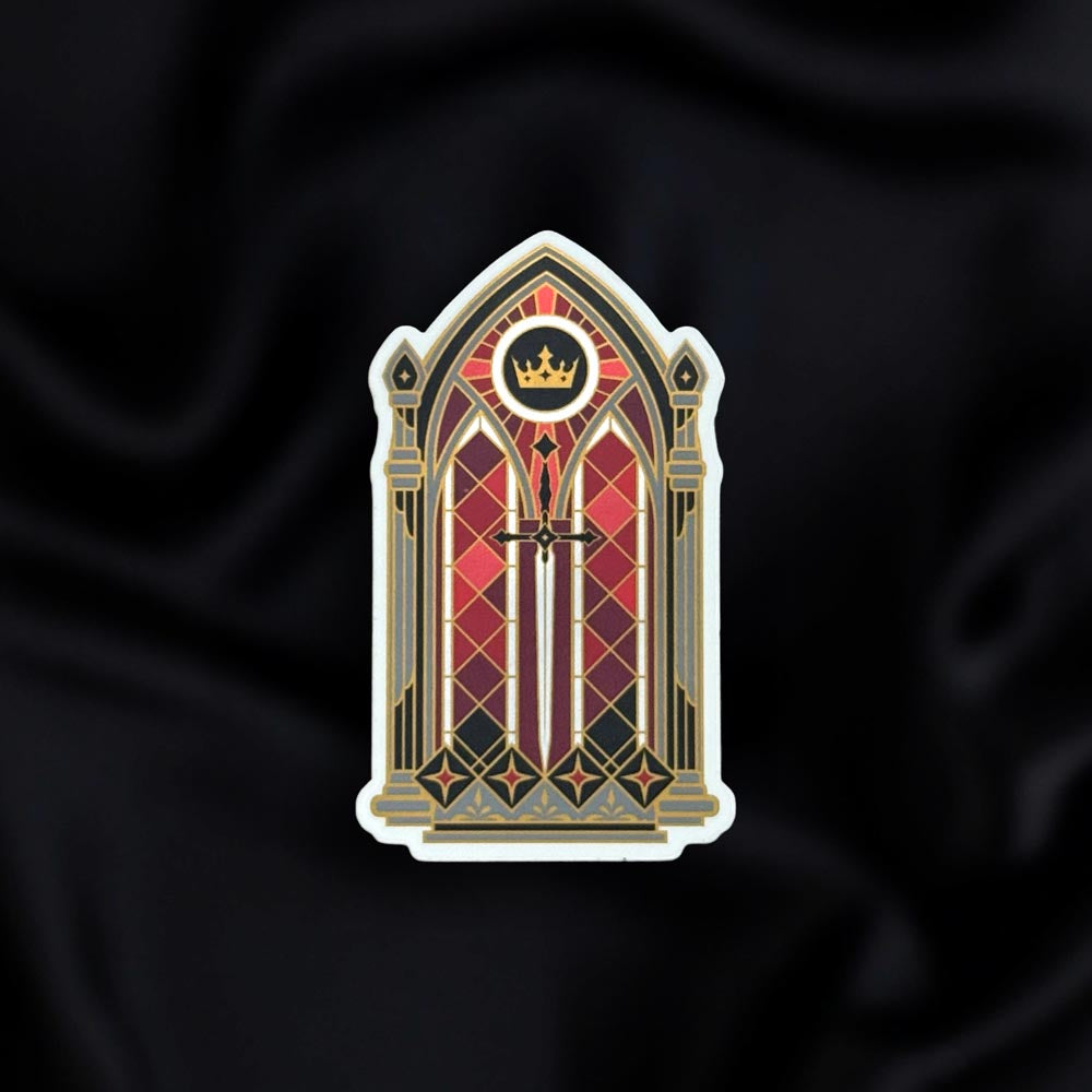 Fractured Fate- a fantasy vinyl sticker by The Quirky Cup Collective as part of the 'Serpents and Swords' collection- sits on a black fabric background. The fantasy book sticker shows a stained glass window with a crown and sword motif in shades of red, silver and black.