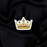 Gilded Heir- a fantasy vinyl sticker by The Quirky Cup Collective as part of the 'Serpents and Swords' collection- sits on a black fabric background. The fantasy book sticker shows a gold grown with white, red and black detailing.