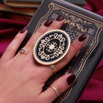 Hand holding a round, decorative clingie MagSafe device grip with intricate designs against a black fabric background.