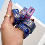 Five rolls of washi tape with blue and purple backgrounds with pink and blue flowers and gold foil