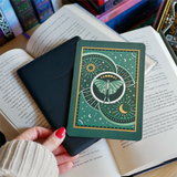 Image shows a hand gently touching a kindle and a kindle sticker insert sitting on top of the device. They sit on a bed of open books. The teal, gold and white design shows a luna moth surrounded by moons, stars and decorative embellishments.