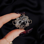 Black and silver hands with magic detailed enamel pin held by a hand against a dark background