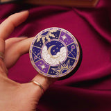 Fingers holding a decorative kindle grip with intricate purple designs with gold accents on a dark fabric background