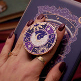 Hand holding a decorative kindle grip with intricate purple and moon designs with gold accents on a dark kindle background
