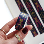 A close up of the Blood Spilledwashi tape by The Quirky Cup Collective. The fantasy book inspired washi tape design is pink, blue with gold detailing with a goblet motif.