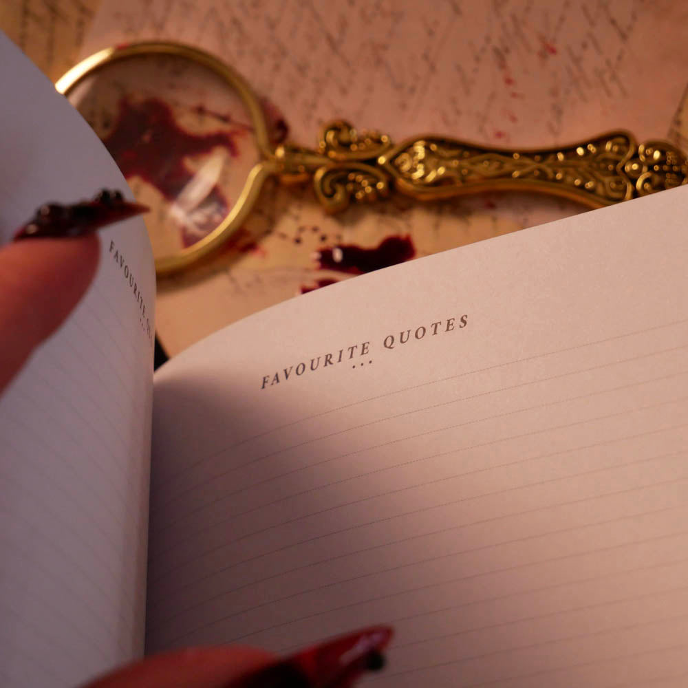 An open Serpents & Swords Reading journal by The Quirky Cup collective shows the 'favourite' reading journal spread. The journal is held open by a hand with intricate red fingernails in a dark and shadowy setting surrounded by handwritten notes and a magnifying glass.