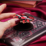 Heart with wings E-reader and phone grip held by a hand with dark nail polish against a black background