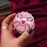 Heart E-reader and phone grip held by a hand with dark nail polish against a pink background