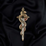 The fantasy book inspired Serpentine enamel pin by The Quirky Cup Collective sits on a black background. The gold pin features black and red detailing and shows a snake curled around a sword alongside a drop of blood.