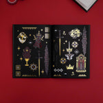 A black paged journal open on a red tabnle shows the Swords and Serpents transparent sticker washi tape by The Quirky Cup Collective. The fantasy book inspired washi tape is red, black, white and fold and functions like a set of individual stickers featuring motifs of snakes, swords, crowns, dragons and more.