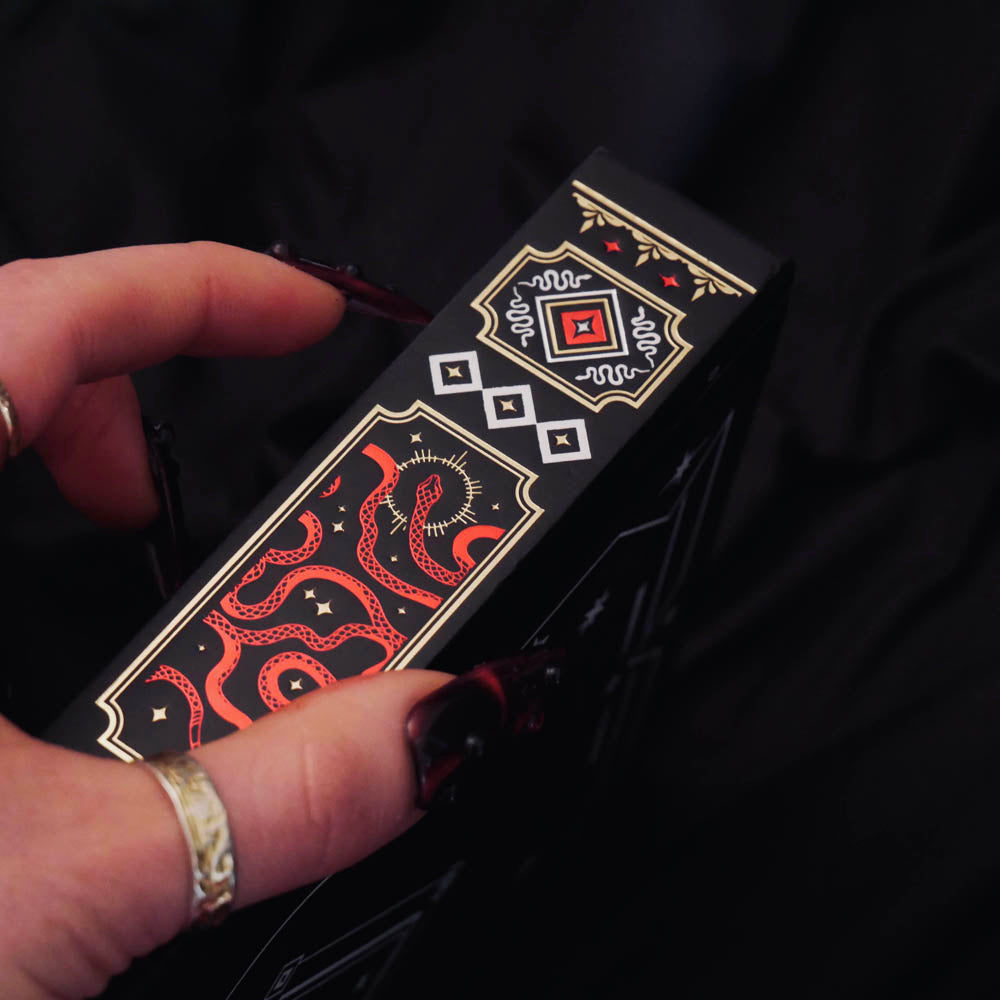 A detail of the Serpents & Swords Reading Journal. The black journal features intricate gold, red and white foiling with motifs inspired by fantasy books such as crowns, swords, goblets and snakes.