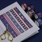 The full set of Serpents and Swords washi tapes, a romantasy book inspired collection by The Quirky Cup Collective, are show on a white journal on a blue table. The five washi tapes are in shades of pink and blue with intricate gold foiling. The designs feature motifs of snakes, crowns, swords, goblets , stars and serpents and perfectly match the fantasy book aesthetic.