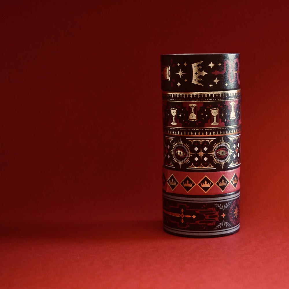 The full set of Serpents and Swords washi tapes, a dark fantasy book inspired collection by The Quirky Cup Collective, are stacked in front of a red backround. The five washi tapes are in shades of red, black and white with intricate gold foiling. The designs feature motifs of snakes, crowns, swords, goblets , stars and serpents and perfectly match the romantasy book aesthetic.