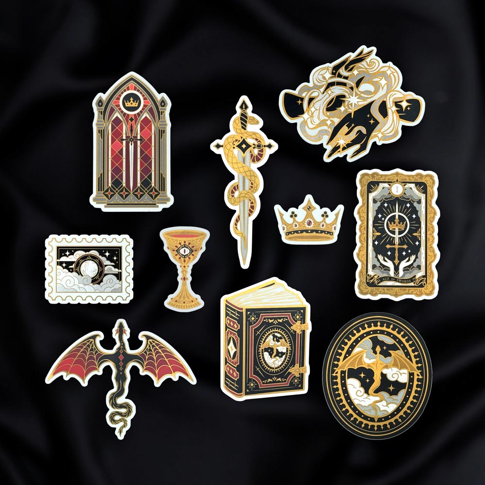 A collection of fantasy book inspired vinyl stickers sit on a black fabric background from The Quirky Cup Collective 'Serpents and Swords' collection. They show motifs of hands, stained glass, dragons, swords and snakes.