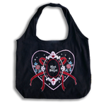 slut for smut tote bag with transparent background. Black cotton bag with red, pink, white and teal embroidery. Design features hearts, stars, leaves, scalloping and bows.