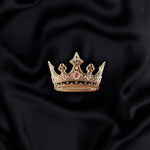 Gold black and red crown enamel pin held by a hand against a dark background