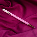 A close up of the You Are Magic pen in bubblegum pink. On a pink fabric background, the pink pen features stars and moons in gold and the phrase 'You are magic' on the gold pen clip.