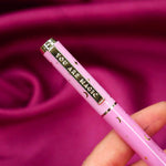 A close up of the You Are Magic pen in bubblegum pink. On a pink fabric background, the pink pen features stars and moons in gold and the phrase 'You are magic' on the gold pen clip.