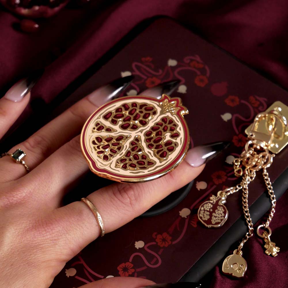 A hand holding Clingie (it's like a bookish pop socket) attached to a kindle with a matching kindle insert sticker and charmlet. 