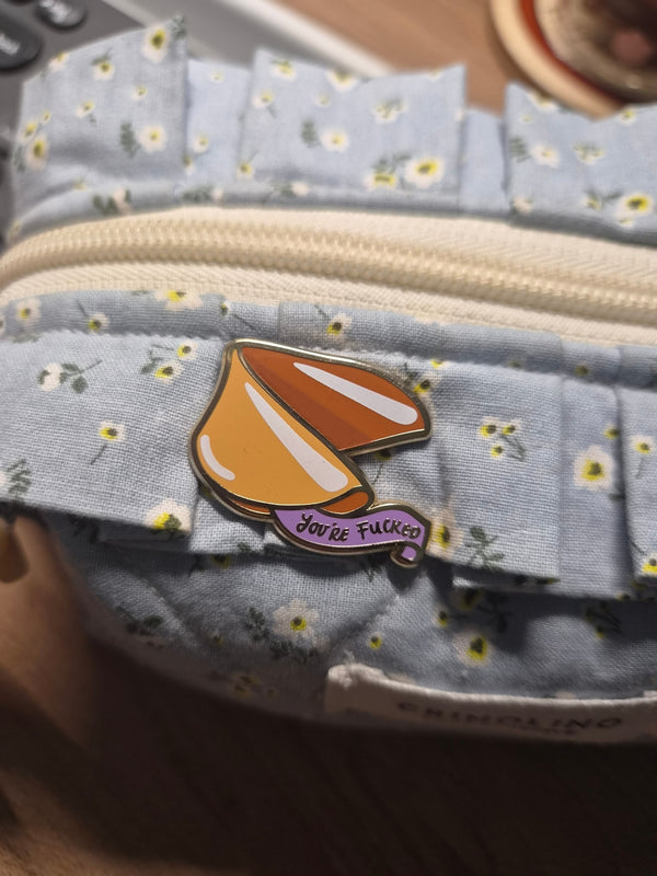 A fortune cookie enamel pin that says 'you're fucked'