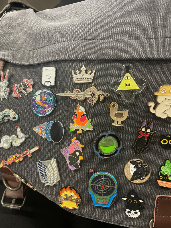 A collection of book fandom inspired enamel pin designs on a pencil case.