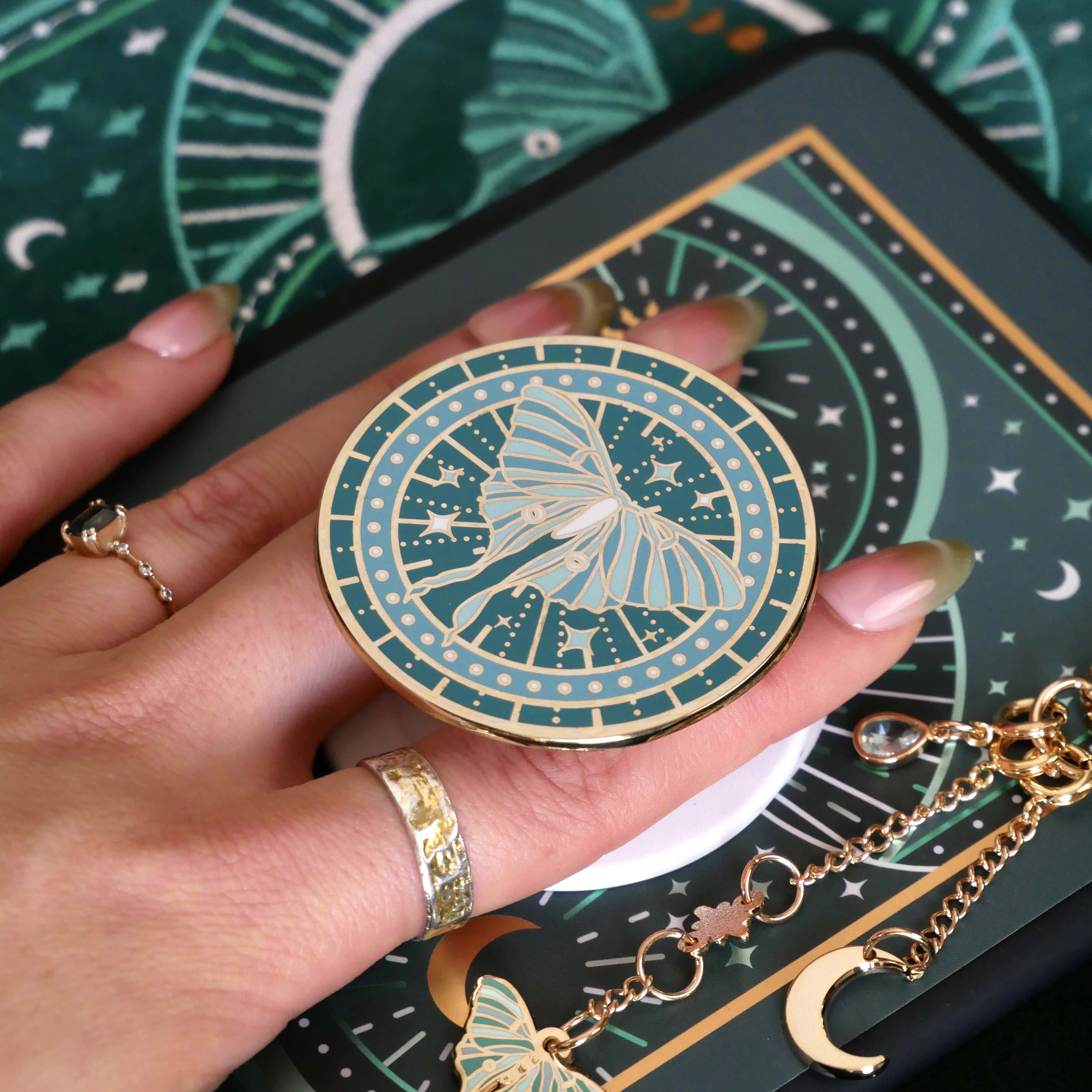 teal clingie depicting a luna moth featuring celestial accents positioned on the back of a kindle and accessories by the quirky cup collective