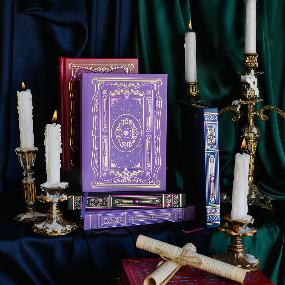 Literati Journals - Set of 4 - The Quirky Cup Collective - Four decorative and gilded classically designed journals in green, purple, blue and red. Stacked with their covers and spines against a silk background with a brass gold candelabra