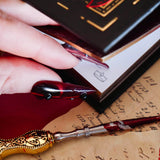 A detail of the corner illustrations of the  Oath Breaker Journal. The journal is surrounded by handwritten notes and features small crown illustrations in the corners. The black journal features intricate gold, red and white foiling with motifs inspired by fantasy books such as crowns, swords, goblets and snakes.
