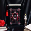 black velvet book sleeve with red, pink and white embroidery sits  in front of a background of draped black satin. Sleeve has a red tassel and a quilted inspired design with stars, hearts, roses and bows. In the centre it says 'slut for smut'. Sleeve sits framed by a candle, books and a rose. 