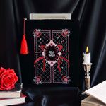 black velvet book sleeve with red, pink and white embroidery sits  in front of a background of draped black satin. Sleeve has a red tassel and a quilted inspired design with stars, hearts, roses and bows. In the centre it says 'slut for smut'. Sleeve sits framed by a candle, books and a rose. 