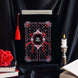 black velvet book sleeve with red, pink and white embroidery sits  in front of a background of draped black satin. Sleeve has a red tassel and a quilted inspired design with stars, hearts, roses and bows. In the centre it says 'slut for smut'. Sleeve sits framed by a candle, books and a rose. 