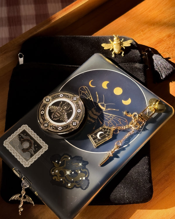 A kindle with a gold and black kindle aesthetic with bee stickers, clingie and charmlet