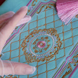 Detail of the intricate embroidery on the front of the Antoinette aqua velvet zippered pouch (aka feminine book sleeve) featuring  gold, pink and cream embroidery detail. The classic literature inspired design is perfect for a feminine french library aesthetic.