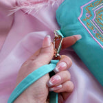 A detail of the aqua Kindle sleeve in Antoinette. The mint green velvet eReader case features pink, cream and gold embroidery with a classic book inspired design. Here a hand shows off the wrist strap with gold detailing.